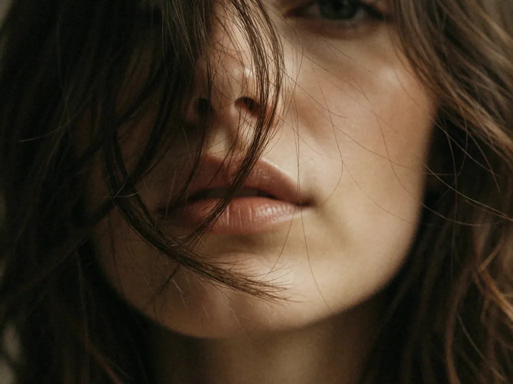 Extreme close-up of a woman's face partially obscured by tousled dark brown hair, soft parted lips, smooth…, made with Krea 2