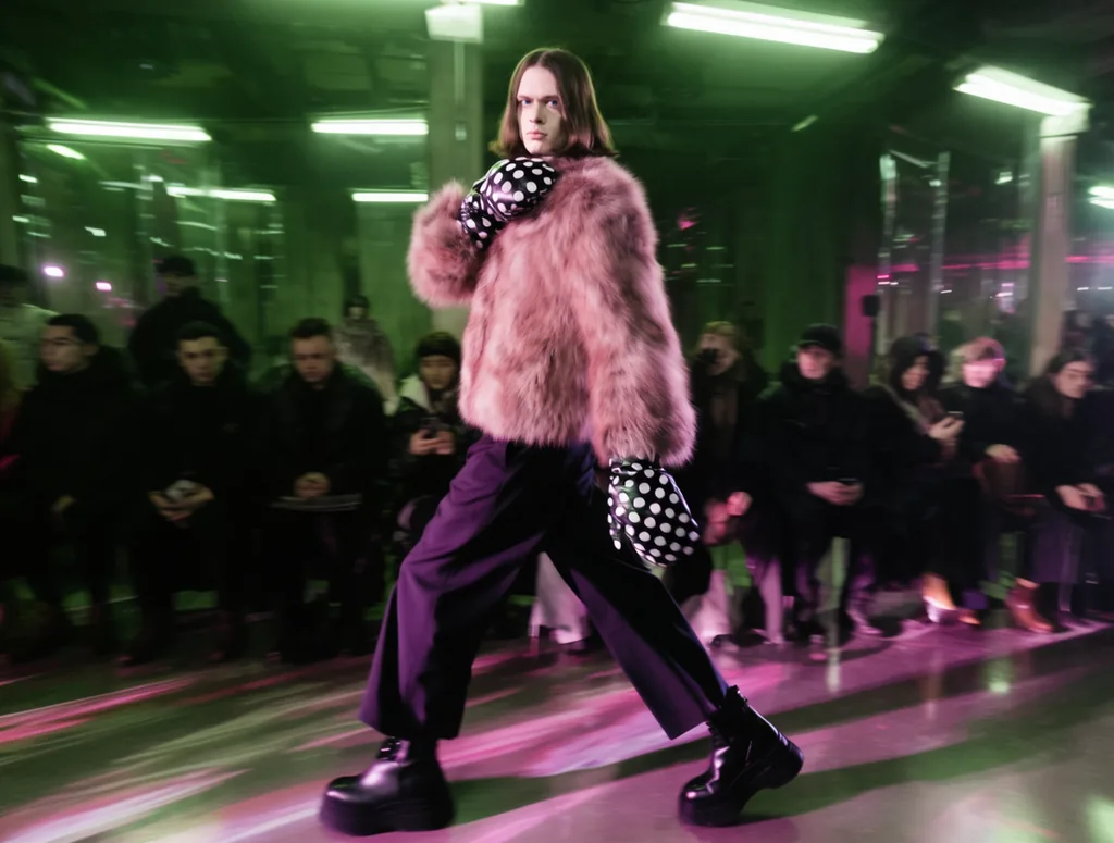 Over-the-shoulder tracking shot of a model walking with exaggerated runway gait — torso twisted unnaturally…, made with Krea 2