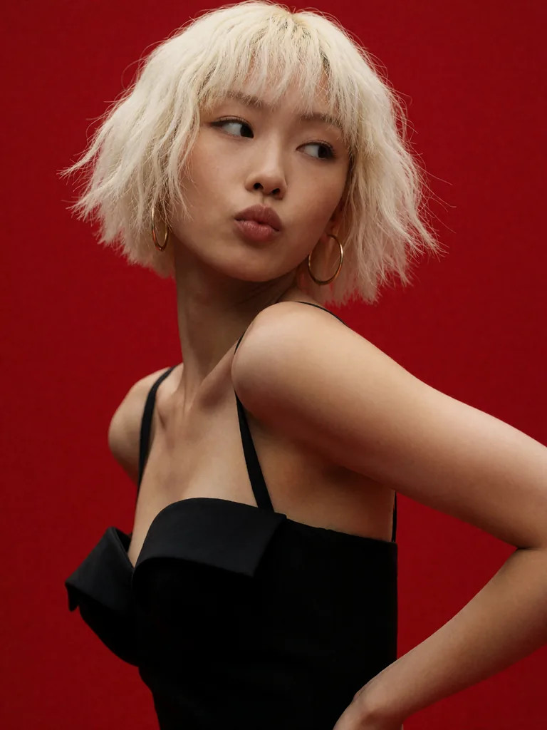 High-fashion editorial portrait of a young East Asian woman, short choppy platinum blonde bob with heavy…, made with Krea 2
