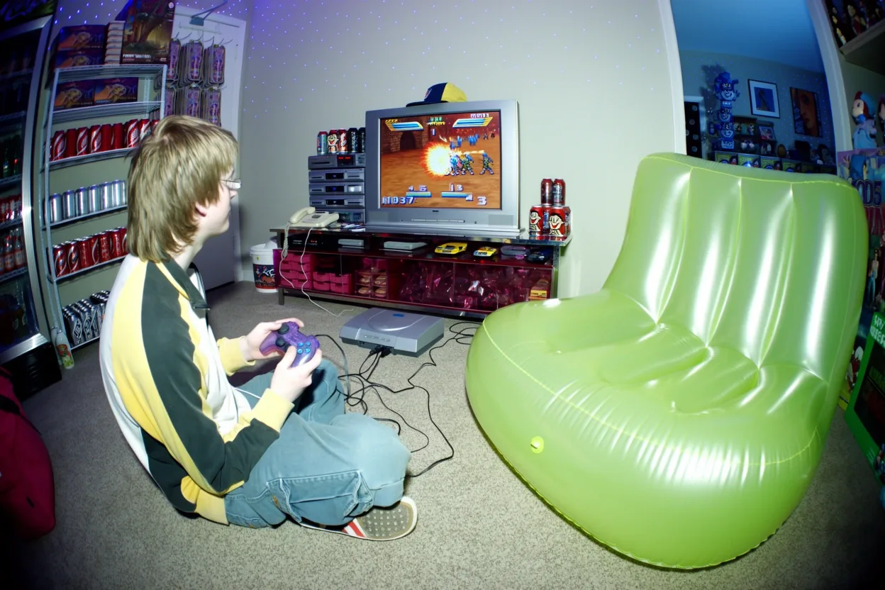 A fisheye flash photo of a teenager playing a video game on a CRT TV beside an inflatable green chair