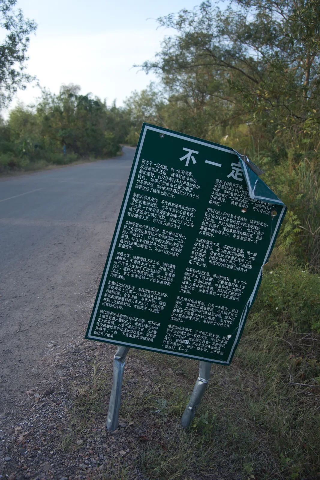 A bent green roadside sign printed with two dense columns of a humorous Chinese essay